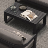 A luxury, kohl-colored aluminium outdoor table with a modern, dark aesthetic, styled alongside the N3 Kohl three-seater sofa in smoke weave and our H3 Fog rug. The sleek table, with its smooth matte finish and clean lines, complements the sophisticated, contemporary design of the sofa and rug, creating an effortlessly chic and cohesive outdoor living space.
