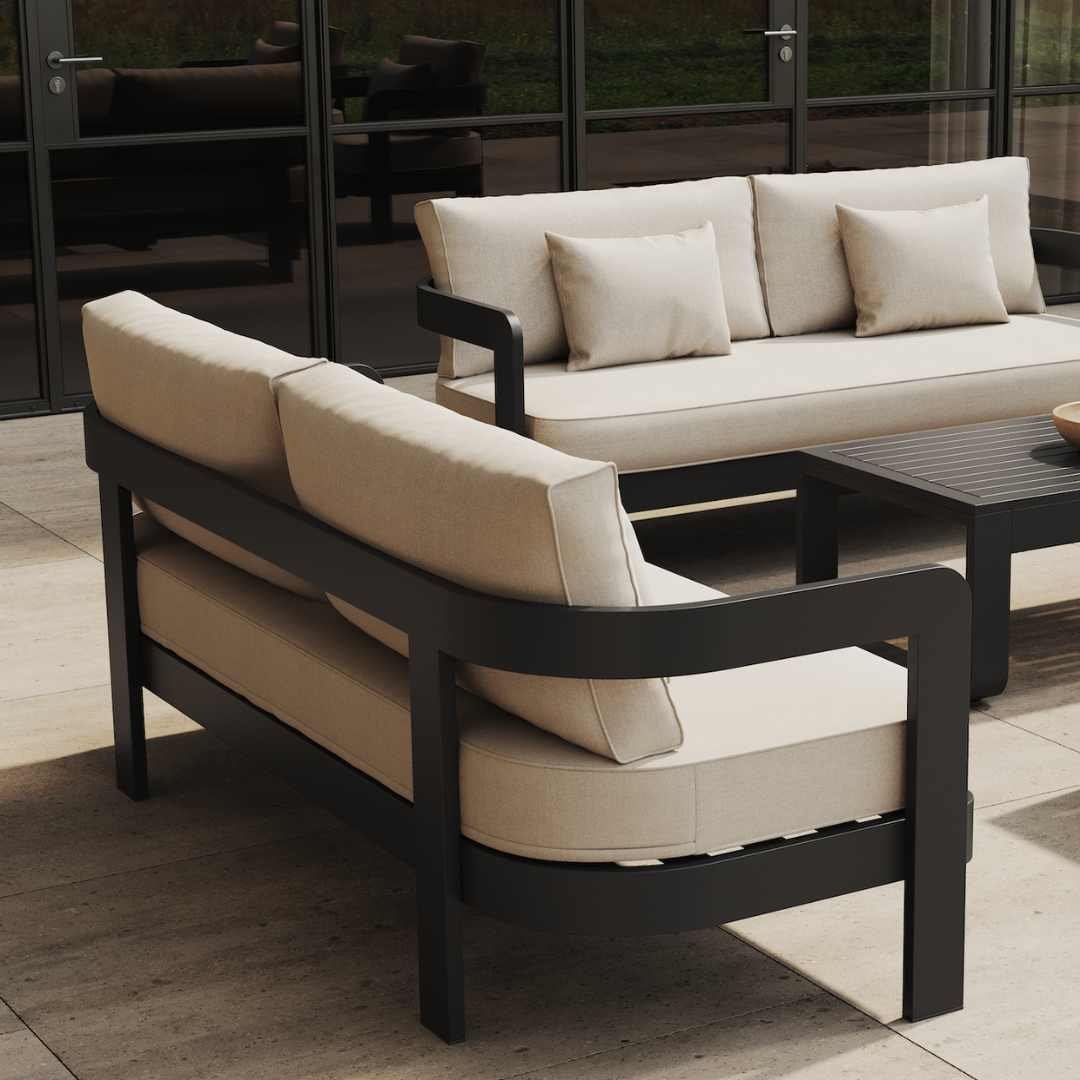 Outdoor lounge area with black aluminum frame sofas with cream cushions, against dark glass doors.
