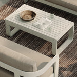 A luxurious stone-coloured outdoor coffee table with a sleek aluminium frame, styled alongside the N3 three-seater sofa in sand canvas fabric and the H1 biscuit rug. The table’s elegant stone finish and modern aluminium frame create a sophisticated focal point, perfectly complemented by the soft, neutral tones of the sofa and rug, forming a refined and inviting outdoor living space.