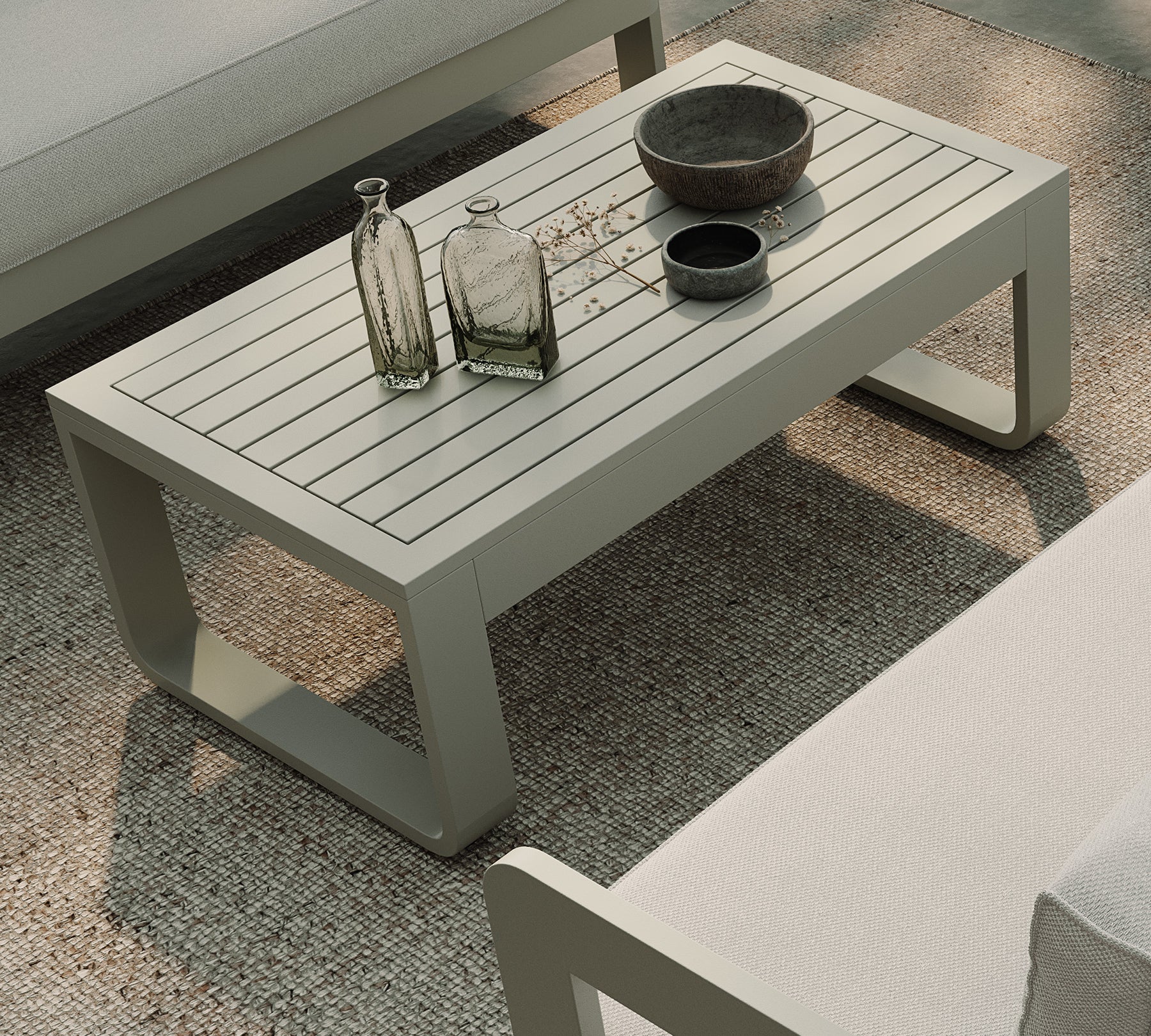 A luxurious taupe aluminium coffee table as the centrepiece of an outdoor setting, paired with a three-seater sofa in Cirrus Textured Weave and a soft Blond rug. The sleek taupe table’s modern design stands out, offering a stylish focal point for outdoor lounging. Its durable material complements the contemporary elegance of the sofa and rug, creating a sophisticated, yet relaxed, outdoor living space.