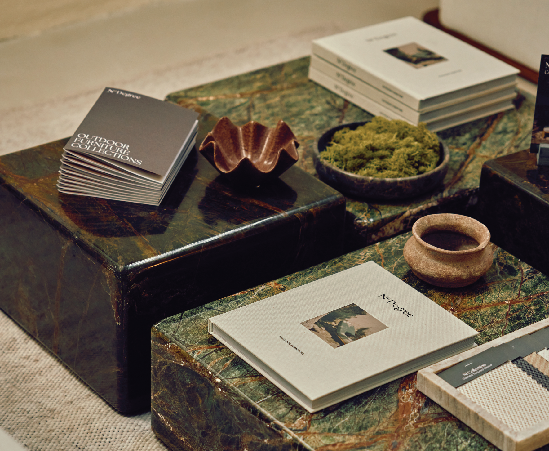 A green cluster of square marble coffee tables, covered in books, brochures and vases