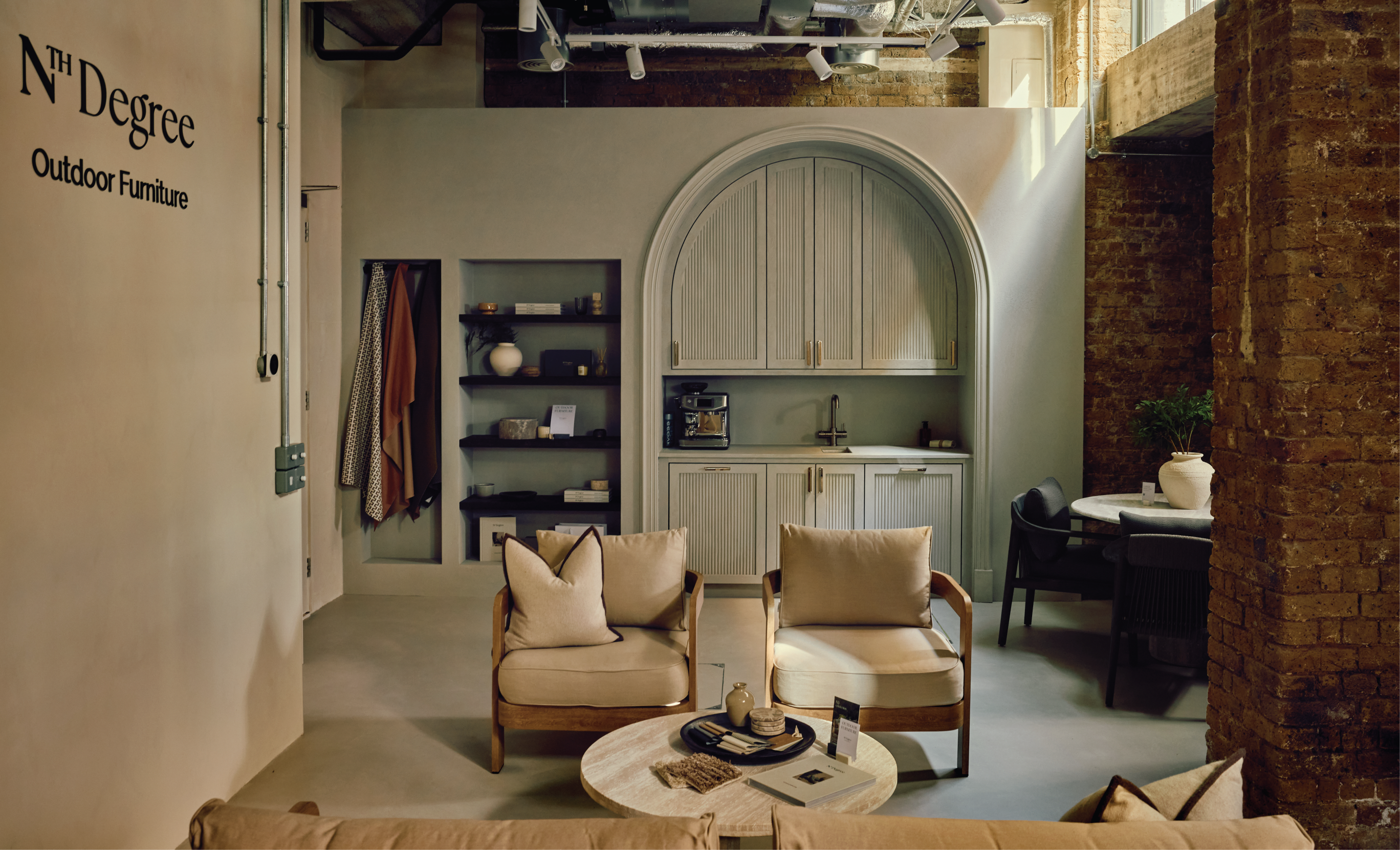 A stylish outdoor furniture showroom with N3 oak lounge chairs, a round coffee table, and a built-in arched kitchenette.

